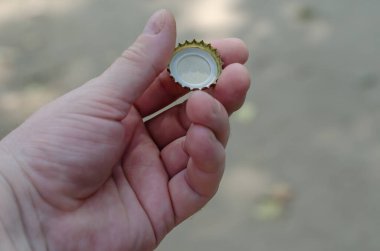 Bir el, bulanık bir arka planda alkolsüz bir içeceğin durdurucusunu tutar. Yuvarlak metal bir şişe kapağı tutan yetişkin bir erkeğin sol eli..