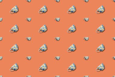 Turuncu arka planda tekrarlanan seramik çay fincanı. Beyaz ve sarı papatyalarla süslenmiş güzel bir kupa. Sıcak içecekler için büyük ve küçük bardaklar..