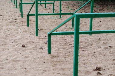 Tekrarlayan yeşil metal bir yapının yakın plan çekimi, kumun içinde geri çekilen bir perspektifte ayarlanmış. Evcil hayvanları eğitmek için özel engeller. Köpek çevikliği. Aktif yaşam tarzları, spor. Gündüz vakti. Hiçbiri.