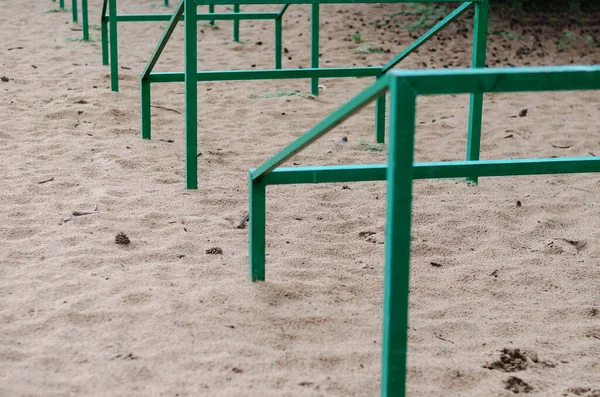 Tekrarlayan yeşil metal bir yapının yakın plan çekimi, kumun içinde geri çekilen bir perspektifte ayarlanmış. Evcil hayvanları eğitmek için özel engeller. Köpek çevikliği. Aktif yaşam tarzları, spor. Gündüz vakti. Hiçbiri.