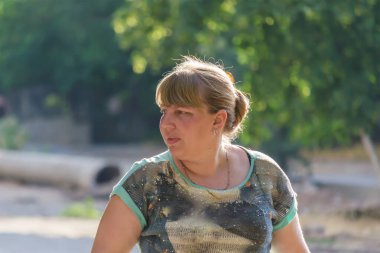 A middle-aged woman walks down a sunny summer street. A grown woman with her hair pulled back.