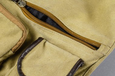 Gri bir arka planda bir omuz çantasının yakın plan görüntüsü. Fermuarlı, kanca ve ilmikle bağlanmış, zeytin rengi bez bir çanta. Giysi aksesuarları.