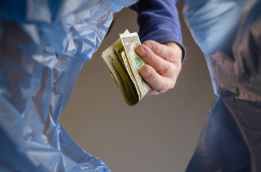 Bir adam çöpe Amerikan doları atıyor. Bir el parayı çöp kutusunun üstünde tutuyor. Alt görünüm.