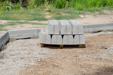 Yeni gri kaldırımlar ahşap bir paletin üzerine yığılmış. Kaldırımlar yol ve kaldırım arasında ayırıcı olarak kullanılır. Yeni bir yolun onarımı ya da inşaatı. Endüstri. Dışarı çıkın. Gündüz vakti. Kimse yok..