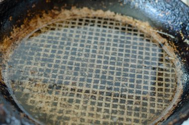 An old frying pan with red-hot cooking oil. Close-up of a cast-iron frying pan with a fluted bottom. Selective focus.