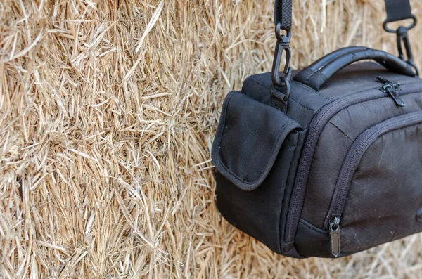 Close-up Black camera bag hanging against a wall of dry straw. A small waterproof camera bag. Warehouse of rectangular bales of hay.