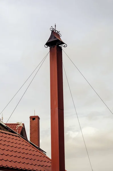 曇った空に対して煙突と赤い屋根 キャップ付きの背の高い煙突は金属製のストレッチャーで揺らされています — ストック写真