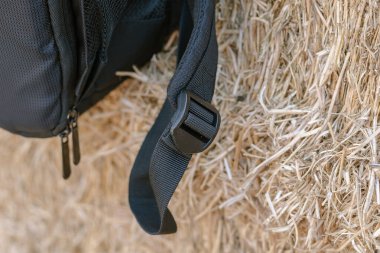 Sırt çantasının siyah kayışını sarı samana yakın çekim. Sırt çantasının kayışını ayarlayan siyah plastik toka. Seçici odaklanma. Defocus, bulanıklık, gürültü, tahıl etkisi