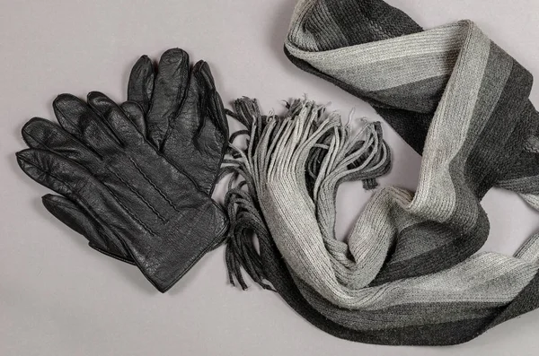 グレーの背景にウールスカーフと革の手袋 ニットの男の黒とグレーの首のスカーフ 暖かいカジュアルウェアアクセサリー トップ表示 — ストック写真