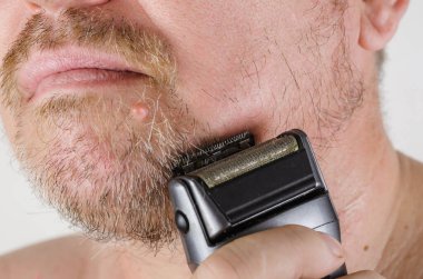Orta yaşlı bir adam yüzünü elektrikli jiletle tıraş eder. Vücut bakımı. Günlük rutin. Tıraş.