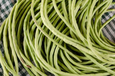 Çiğ yeşil fasulye kabukları yakın plan. Beyaz ve yeşil kareli tekstil önünde uzun, çiğ kuşkonmaz tohumları. Sağlıklı yiyecekler. Seçici odak.