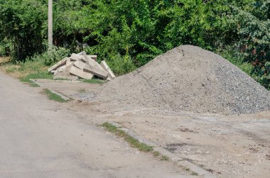 Yolun kenarına yığılmış bir çakıl yığını ve eski beton kaldırımlar. Arka planda yeşil dut ağaçları bulanıklaştı. Gündüz vakti. Yaz.