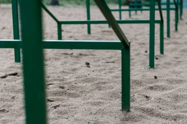 Tekrarlayan yeşil metal bir yapının yakın plan çekimi, kumun içinde geri çekilen bir perspektifte ayarlanmış. Evcil hayvanları eğitmek için özel engeller. Köpek çevikliği. Aktif yaşam tarzları, spor. Gündüz vakti. Hiçbiri.