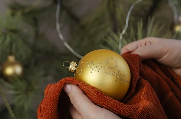 女がクリスマスボールをむしり取る 大人の女性は茶色の布で黄金のクリスマスツリーボールを拭くことです 新年とクリスマスの休日 選択的焦点 — ストック写真