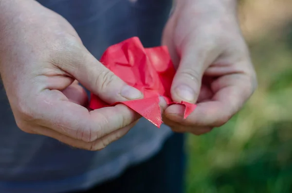 Un hombre rompe nerviosamente un trozo de papel rojo. Manos sosteniendo una mojada —  Fotos de Stock