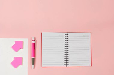 Kağıt sayfaları, açık defter, ok yer imleri, pembe torba üzerindeki kalem.