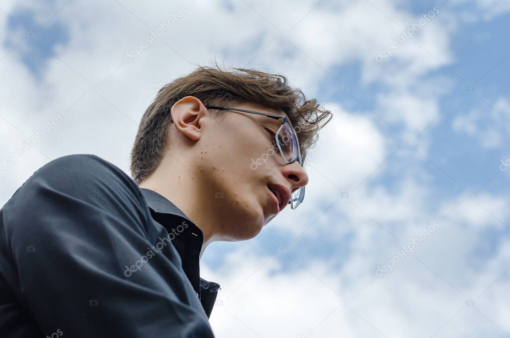 A portrait of a young adult male against a blue sky. A man weari