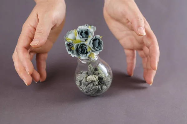 Womans hands cover an electric lamp with artificial flowers on