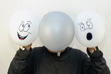 Bir adam yüzünün önünde üç balon tutar. İki beyaz balo