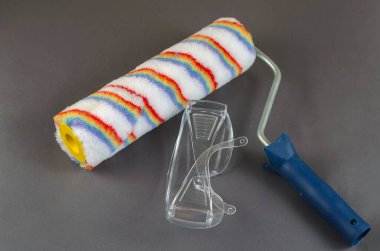 Gri arka planda yeni boya silindiri ve güvenlik gözlükleri. Elini de.