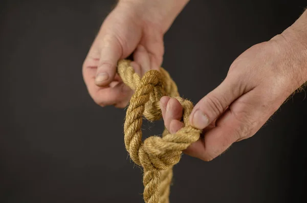 Homem amarra nó contra fundo preto. Mãos segurando jut amarelo — Fotografia de Stock