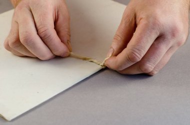 Belge klasörüne iki elle düğüm atılıyor. Gri üzerine kağıt klasörü