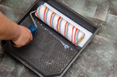 Bir kadın boya silindirini ıslatıyor. Duvar döllenmesi.