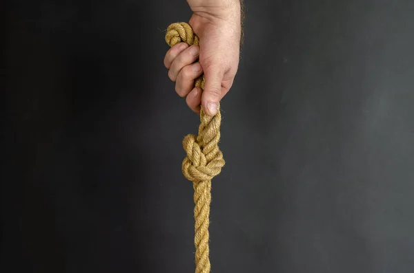 Adult Male holds vertically a rope with a knot. Hand holds a yel — Stock Photo, Image