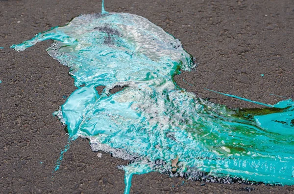 Blue-green paint spilled on the asphalt. Oil-based paint spreadi