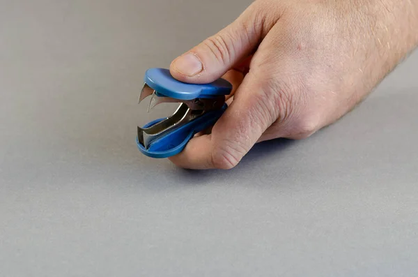 Hombre mantenga azul removedor de grapas contra el fondo gris. Dispositivo tha — Foto de Stock