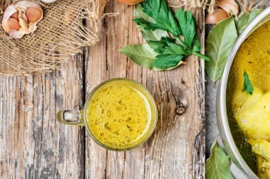 Tavuk çorbası cam bardağa dökülür. Çorba ve ahşap bir masada çorba için malzemelerle dolu bir tava. Çorbalı bir kupa ile bir masanın üst görüntüsü