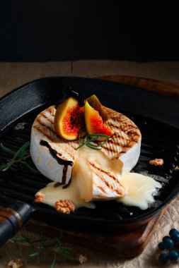 Dökme demir tavada peynir, incir, ceviz ve biberiyeyle pişirilmiş fırın. Yakın plan, siyah arkaplan