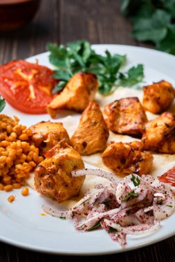 Hafif ve lezzetli ızgara tavuk kebabı, domates ve bulgur dolu bir tabakta, kişniş filizi ile süslenmiş. Sağlıklı ve lezzetli doğu mutfağı. Yakın çekim, alan derinliği