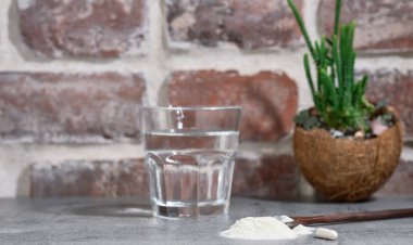 Kolajen Protein Tozu. Hidrolize edilmiş, tahta kaşıkla taş masada, bir bardak suyun yanında. Ek protein alımı. Derinin, kemiklerin ve eklemlerin güzelliği ve sağlığı için doğal destek. Yakın plan.