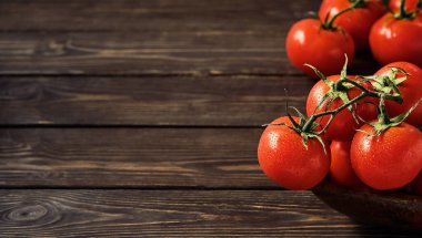 Koyu ahşap arka planda olgun sulu domates dalları. Kopya alanı olan taze domatesler. Su damlalarındaki domatesler.