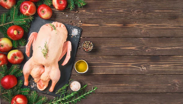 Elma ve baharatlı bir kabın içinde çiğ ördek. Ahşap bir masanın üzerindeki malzemelerin yerleşimi. Noel ya da yeni yıl için şenlikli bir yemek tarifi. Kopyalama alanı olan üst görünüm