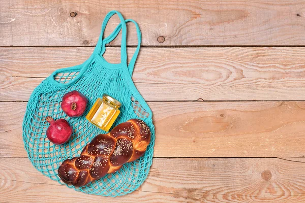 Cloth bag with pomegranates, honey and challah, reusable material for natural products. Zero waste concept. Hanukkah. Conscious consumption concept without plastic waste. Layout, wood background