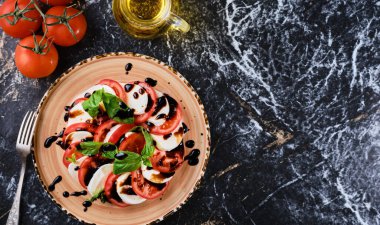 Tomatoes and mazzarella, Italian Caprese salad with tomatoes, mozzarella cheese, basil balsamic vinegar and olive oil. Dark marble background, top view, Vegetarian dish