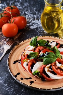 Domates ve mozzarella - vejetaryen yemeği, domatesli İtalyan Caprese salatası, mozzarella peyniri, fesleğen, balzamik sirke ve zeytinyağı. Seramik tabakta. Yakın çekim, seçici odak, mermer koyu masa