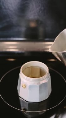 Metal bir İtalyan kahve demliğinde espresso yapıyorum. Temiz su, sobanın üzerinde bulunan bir moka tenceresine dökülüyor. Yakın plan, seçici bir odak noktası. Kahve yapan kafe, barista işyeri konsepti.