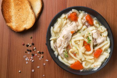 Ev yapımı tavuklu şehriye çorbası, sebze ve baharatlarla dolu bir kâse, üst manzara, ahşap arka plan. Sağlıklı gıda konsepti