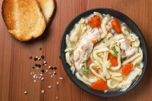 Ev yapımı tavuklu şehriye çorbası, sebze ve baharatlarla dolu bir kâse, üst manzara, ahşap arka plan. Sağlıklı gıda konsepti