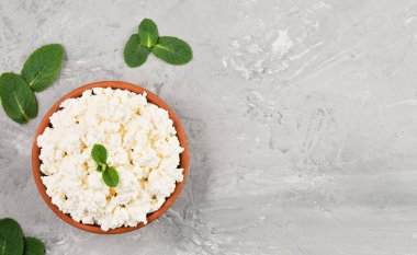 Gri tarafsız arka planda kilden bir kasede ev yapımı doğal süzme peynir, fotokopi alanı olan üst manzara. Yumuşak, doğal, sağlıklı yiyecekler, sağlıklı diyet yiyecekler.