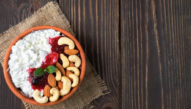 Ekşi kremalı kıtır kıtır süzme peynir, kızılcık reçeli ve ahşap arka planda geleneksel kil kasede fındık. Kaymak tabakasından yapılmış sağlıklı bir kahvaltı, fotokopi alanı olan üst manzara.