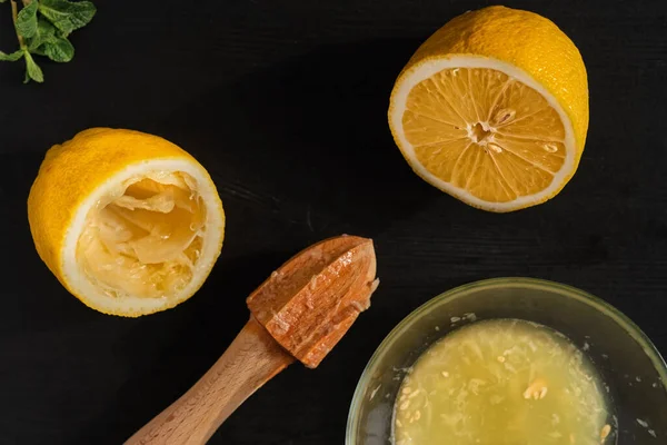 Lemon halves on a black wooden table, making lemon juice with a manual juicer, top view