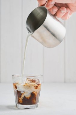 Buzlu kahve gri beton bir masada, kremayı döküyor, desen ve içkinin ferahlatıcı görüntüsünü sergiliyor. Soğuk kahveye yakın çekim, seçici odaklanma, dikey çerçeve