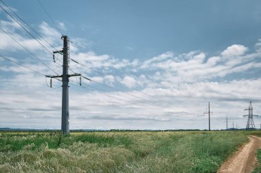 High voltage power lines, landscape on a green field at noon, bright sunny day, blue sky with clouds. Energy supply for urban life