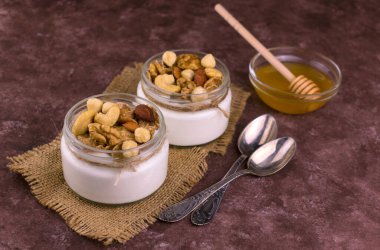 Kahverengi arka planda fındıklı ve ballı küçük kavanozlarda Yunan yoğurdu.