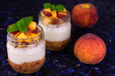 Şeftalili yoğurt ve koyu mavi arka planda küçük kavanozlarda nane..