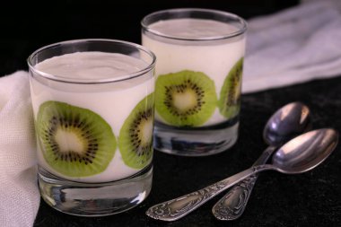 İki bardak yoğurt ve siyah arka planda kivi..